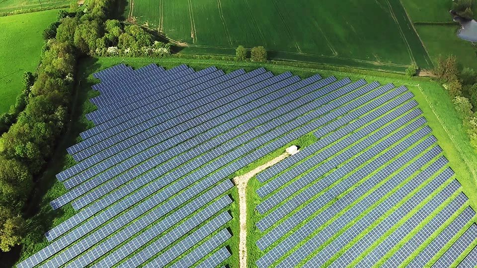 Green agriculture fields and Solar Energy Farm with many Photovoltaic Panels in an aerial view.