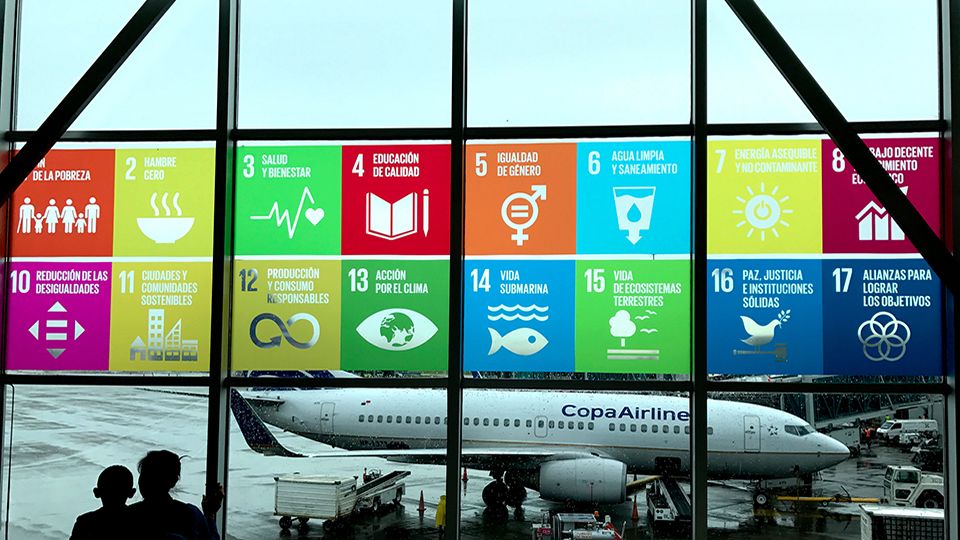 The Global Goals displayed in Spanish on the windows at Panama City Tocumen International Airport. Mother and child looking out to see the planes.