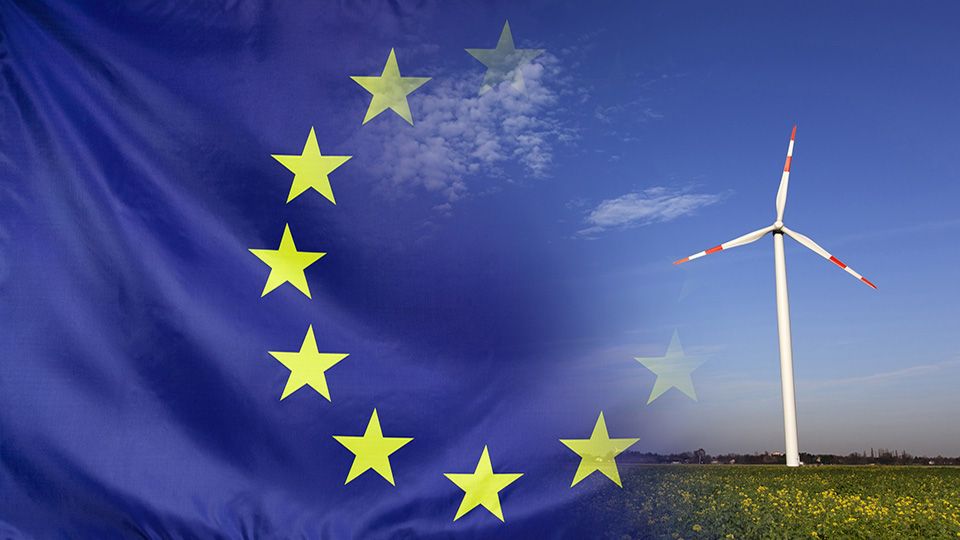Concept clean energy with flag of Europe merged with wind turbine in a blue sunny sky and green grass with flowers