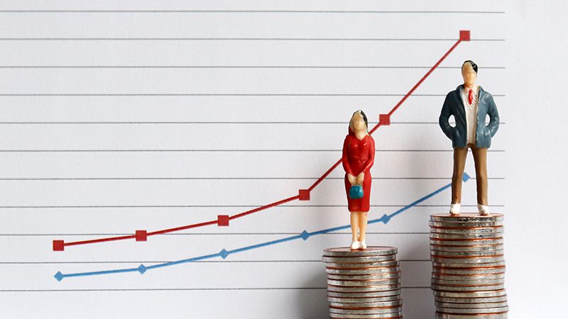 Miniature people standing on a pile of coins in front of a graph. The concepts of continuing gender inequality.