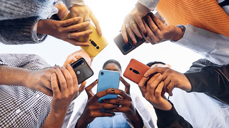 Gen Z circle holding smart mobile phones - Multicultural young people using cellphones outside