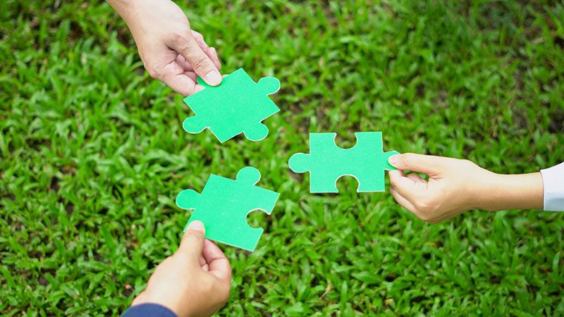 Close-up hand business people of teamwork colleague holding puzzle pieces in a day outdoors on green grass, and green jigsaw copy space for your text use. Team Concept. Top view