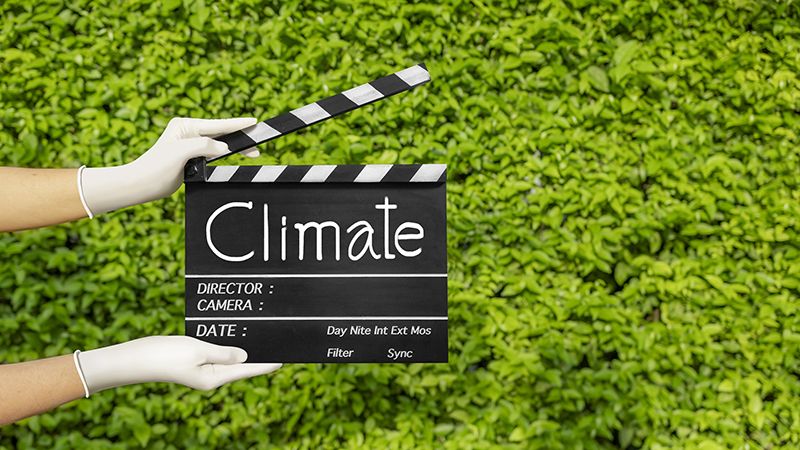 Hands holding film slate or movie clapper board on plant-green nature.Climate change concept.