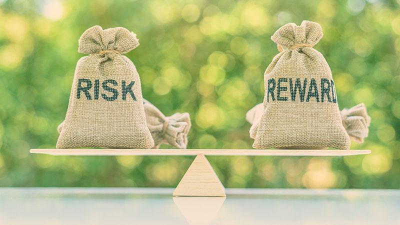 Risk reward ratio / risk management concept : Risk and reward bags on a basic balance scale in equal position, depicts investors use a risk reward ratio to compare the expected return of an investment