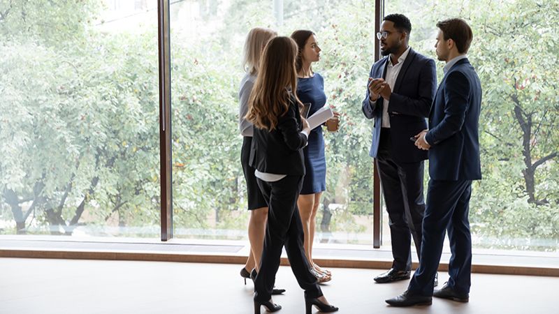 Group of multiethnic managers or employees standing in modern office hall after staff briefing and discussing corporate news, diverse business teammates gather together to share information and plans