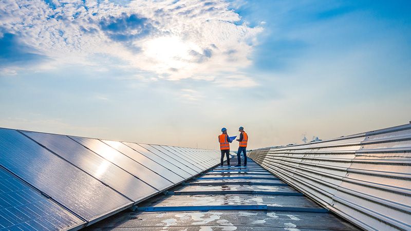 Two technicians in distance discussing between long rows of photovoltaic panels. Alternative energy source, ecology and carbon footprint reduction concept.