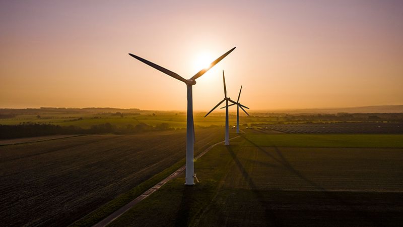 Three large wind turbines at sunrise taken from the air