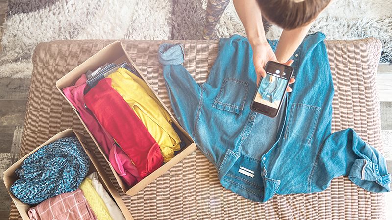 Woman taking photo of denim shirt on smartphone to sell it on internet shop.