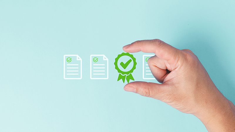 A hand holding green certificate of excellence with check mark icon surround by checklist documents with green check mark for correct and approval concept in pastel blue background.